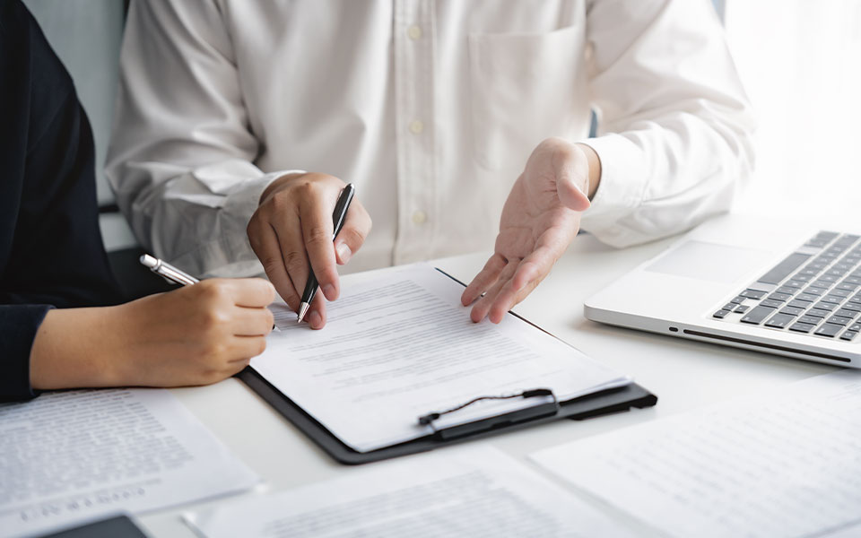 Zwei Personen beim Unterzeichnen eines Vertrags mit Unterlagen, Stift und Laptop auf dem Tisch